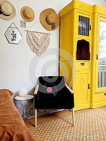 Young woman in beret sits in an armchair in cozy home, in room with music record in hands. Drinking wine. Vintage yellow cabinet Editorial Stock Photo