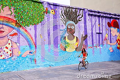 Young woman biking along colorful wall in Montevideo, Uruguay Editorial Stock Photo