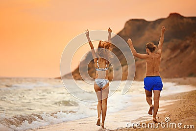 Young woman in bikini and her walking on beach at sunset. Lovely couple Stock Photo
