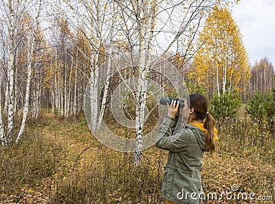 Young woman with binoculars watching birds in the autumn forest. Scientific research Stock Photo