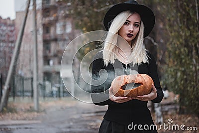 Young woman in the black coat holding the halloween pumpkin with the white smoke coming from inside of it in the autumn Stock Photo