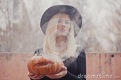 Young woman in the black coat holding the halloween pumpkin with the white smoke coming from inside of it in the autumn Stock Photo