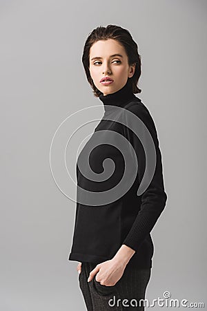 Young woman in black jumper standing with hands in pockets on grey Stock Photo