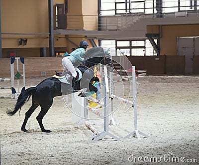 Young woman on the black stallion jumping over hurdle at show jumping competition Editorial Stock Photo