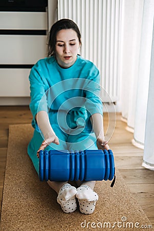 Young woman in blue clothing using foam roller for myofascial release and muscle tension relief. Physical therapy Stock Photo