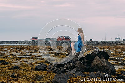 Young woman in blue dress sitting on stone among algae in tide Stock Photo