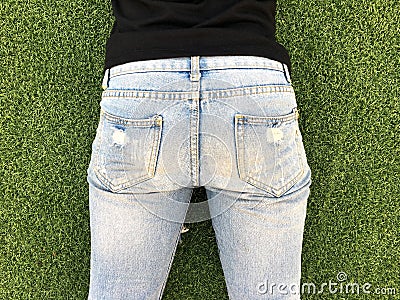 Young woman bottom in light blue jeans in front of green grass background. Stock Photo