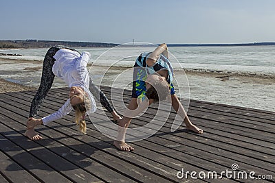 Young woman and boy doing wide legged Forward Bend, twist variation. Stock Photo