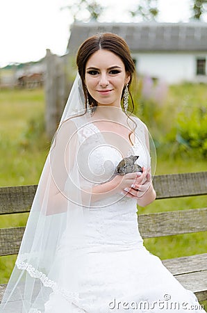 Young woman bride smiling and holding cute rabbit over park summer nature outdoor. White wedding dress, green background Stock Photo