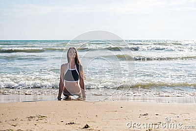 Young woman bruenette in bikini does Bhujangasana yoga asana or Cobra Pose on the sunny beach. Stock Photo