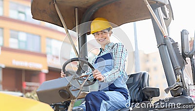 Young woman builder in hard hat sitting behind wheel of asphalt paver Stock Photo