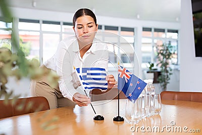 Young woman putting Greece and New Zealand flags on table in office Stock Photo