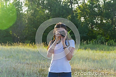 Young woman with camera lens. A beautiful brunette photographer is taking pictures in nature on a summer day Stock Photo