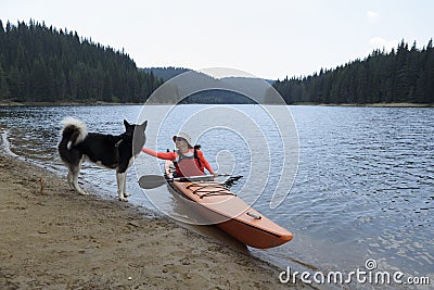 Young woman caress Alaskan Malamute sitting in her kayak Stock Photo