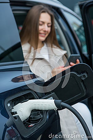 Young woman charging her electric car at a charging station in the city. Stock Photo