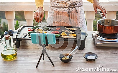 Young woman chef cooking outdoor while streaming online for webinar masterclass lesson at home - Girl making videos preparing Stock Photo