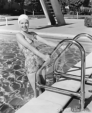 Young woman climbing up the ladder of a swimming pool Stock Photo
