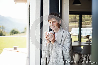 A young woman with coffee standing by patio door at home. Stock Photo