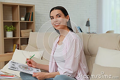 Young woman coloring antistress page on sofa in living room Stock Photo