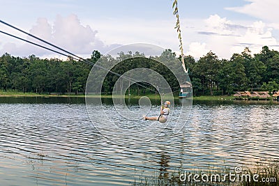 Young woman crossing a lake in zip line in Chiang Mai Stock Photo