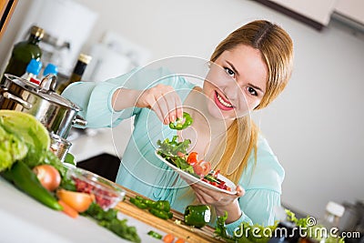 Young woman decorating salad with herbs in kitchen Stock Photo