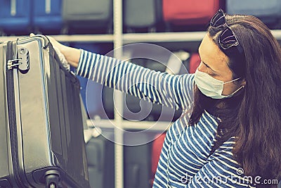 A young woman in a disposable mask choosing a suitcase for the upcoming vacation after the end of the Covid-19 coronavirus Stock Photo