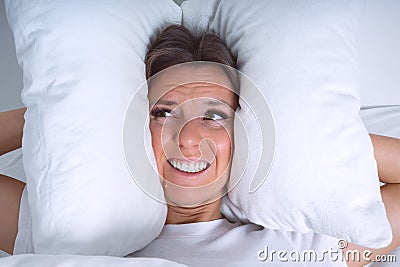 Young woman disturbed by noisy neighbours. Woman struggling from noise in bed and covering ears with pillows Stock Photo