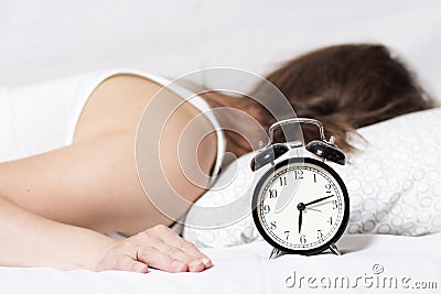 Young woman does not hear ringing of an alarm clock in the morning. The girl does not want to get up early in the morning to work. Stock Photo