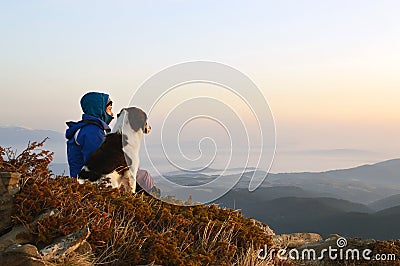 Young woman and dog admiring sunrise high in the mountain Stock Photo