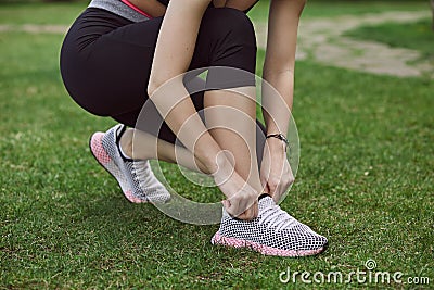A young woman doing exercises outdoors on green grass. Fitness sporty girl tightening her sneakers Stock Photo