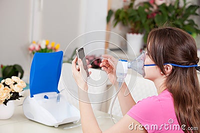 Young woman doing inhalation with a nebulizer at home. dials the doctor`s number for a consultation Stock Photo