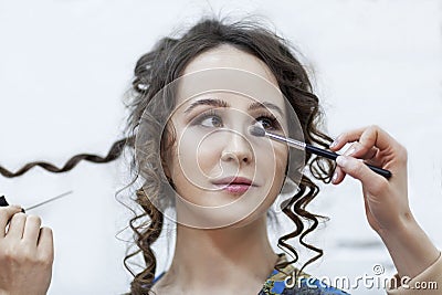 A young woman is doing make-up. Bright brunette with curly hair. Beauty industry. Close-up. Light background Stock Photo