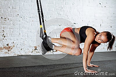 Woman doing push-ups while legs hanging on trx Stock Photo
