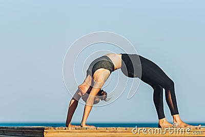 Young woman doing yoga bridge exercise on the beach in front of the sea Stock Photo