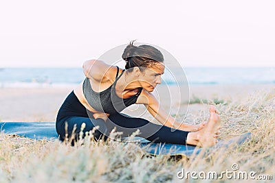 Young woman doing yoga exercise on the ground outdoors by the sea Stock Photo