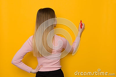 Young Woman Is Drawing On A Yellow Wall, Rear View Stock Photo