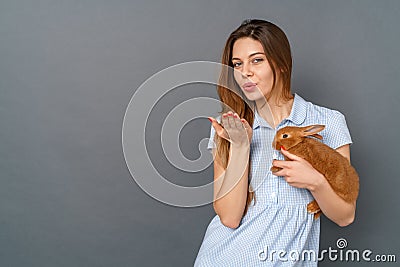 Young woman in dress studio on gray with little bunny sending air kiss Stock Photo