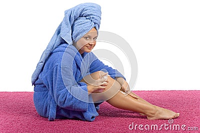 Young woman dressed blue bathrobe rubbing cream into her leg Stock Photo