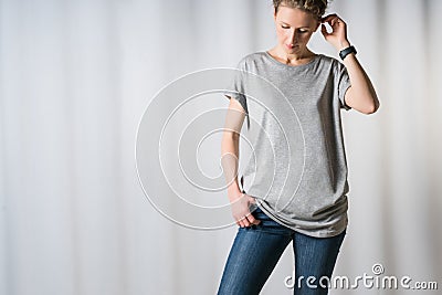 Young woman,dressed in gray t-shirt and blue jeans, standing on light gray background with his hand in pocket of jeans. Stock Photo