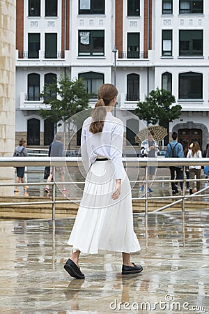 A young woman dressed in white, walks on the pavement wet Editorial Stock Photo