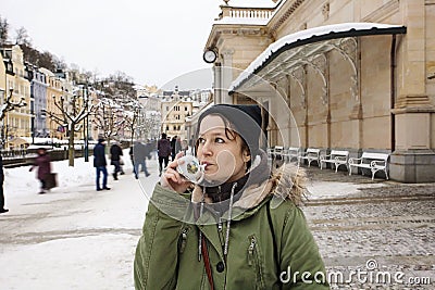 Young woman drinking from cup with therapeutic mineral water at a natural hot spring in Karlovy Vary during winter time Stock Photo