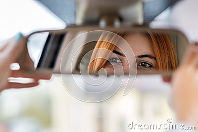 Young woman driver checking rear view mirror looking backwards while driving a car Stock Photo