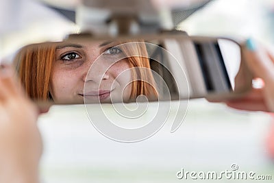 Young woman driver checking rear view mirror looking backwards while driving a car Stock Photo