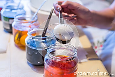 Young woman dyeing Easter eggs at home in the kitchen in the cucumber glass and with different colors, Germany Stock Photo