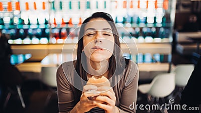 Young woman eating fatty hamburger.Craving fast food.Enjoying guilty pleasure,eating junk food.Satisfied expression.Breaking diet Stock Photo