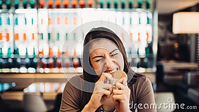 Young woman eating fatty hamburger.Craving fast food.Enjoying guilty pleasure,eating junk food.Satisfied expression.Breaking diet Stock Photo