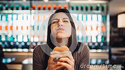 Young woman eating fatty hamburger.Craving fast food.Enjoying guilty pleasure,eating junk food.Satisfied expression.Breaking diet Stock Photo