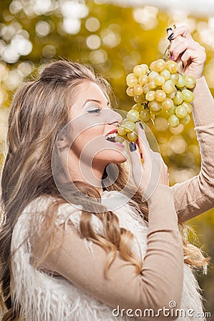 Young woman eating grapes outdoor. Sensual blonde female smiling holding a bunch of green grapes. Beautiful fair hair girl Stock Photo