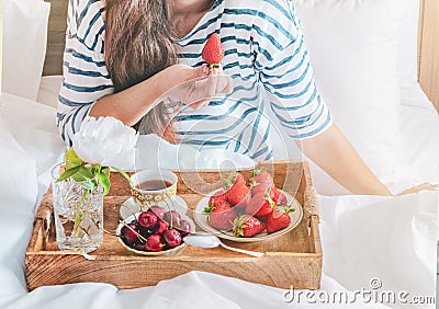 Young woman eating healthy breakfast in bed. Romantic breakfast with strawberries and sweet cherry in a bed Stock Photo