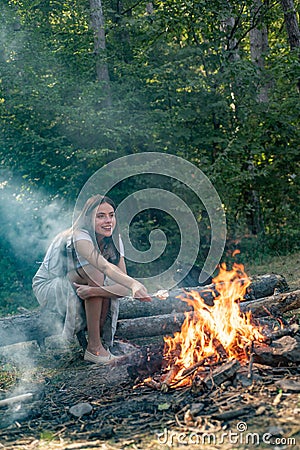 Young woman eating roasted marshmallows while camping near the lake. Woman roasting marshmallows near bonfire. Young Stock Photo